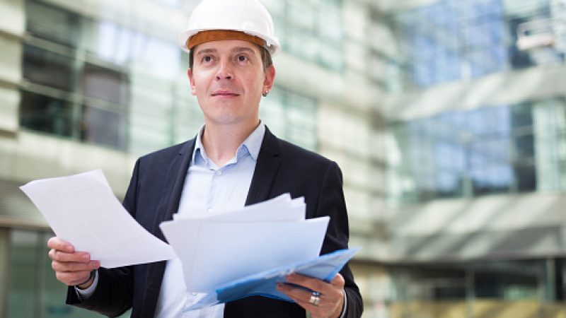 Smiling male architect in helmet with paper documents in the hand